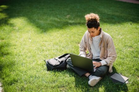From above of focused young male student sitting on green grass while using netbook for studies