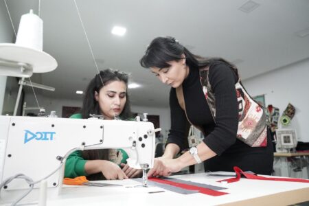 Two women collaborate on a sewing project in a modern workshop, focusing on fabric design.