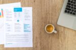 Top view of a desk with resume, coffee cup, and laptop on a wooden surface, ideal for business concepts.