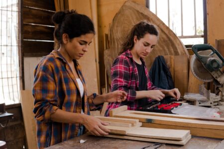 Two women working together in a carpentry workshop with tools and materials.